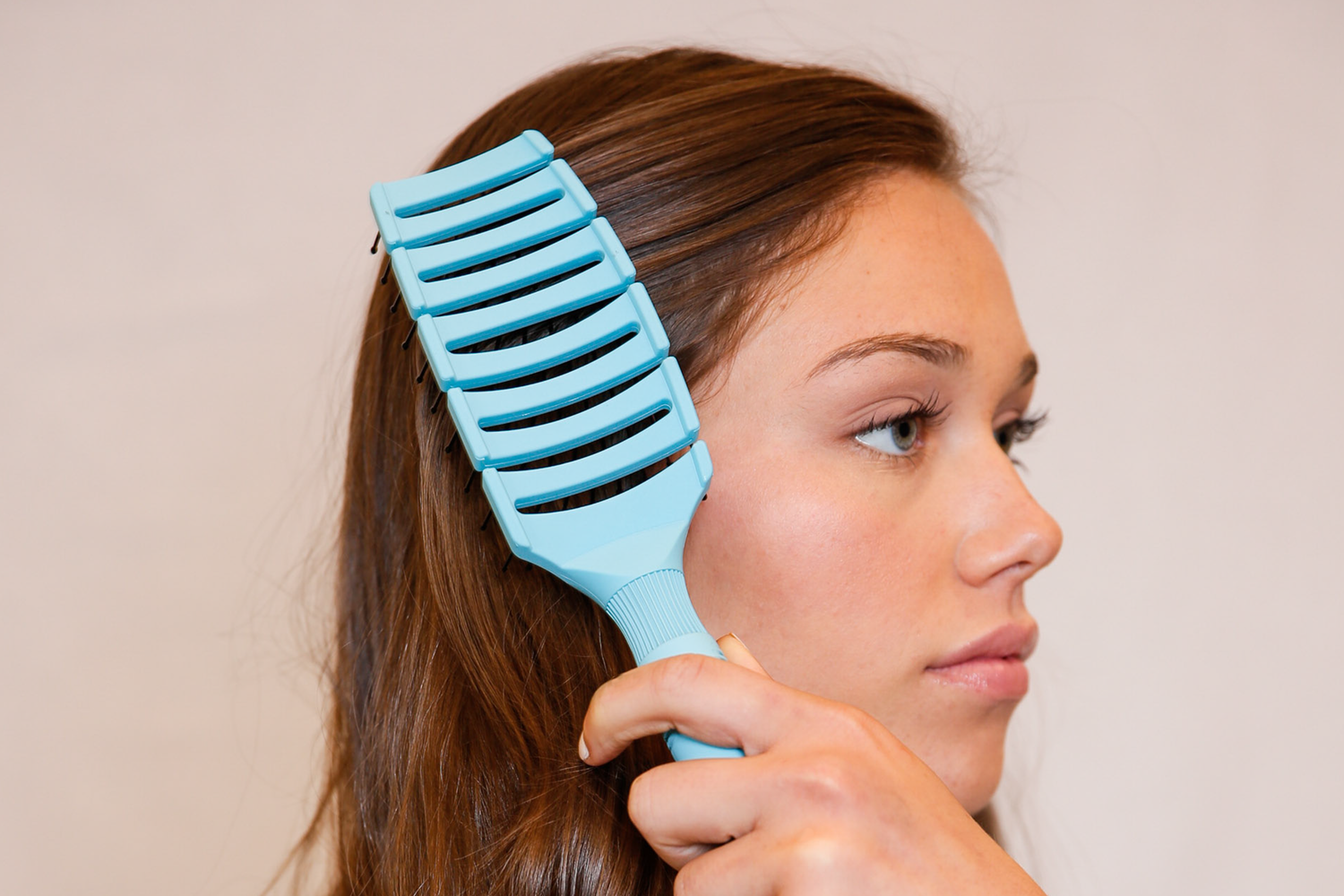 Brown haired woman brushing her hair with a blue Flex Brush
