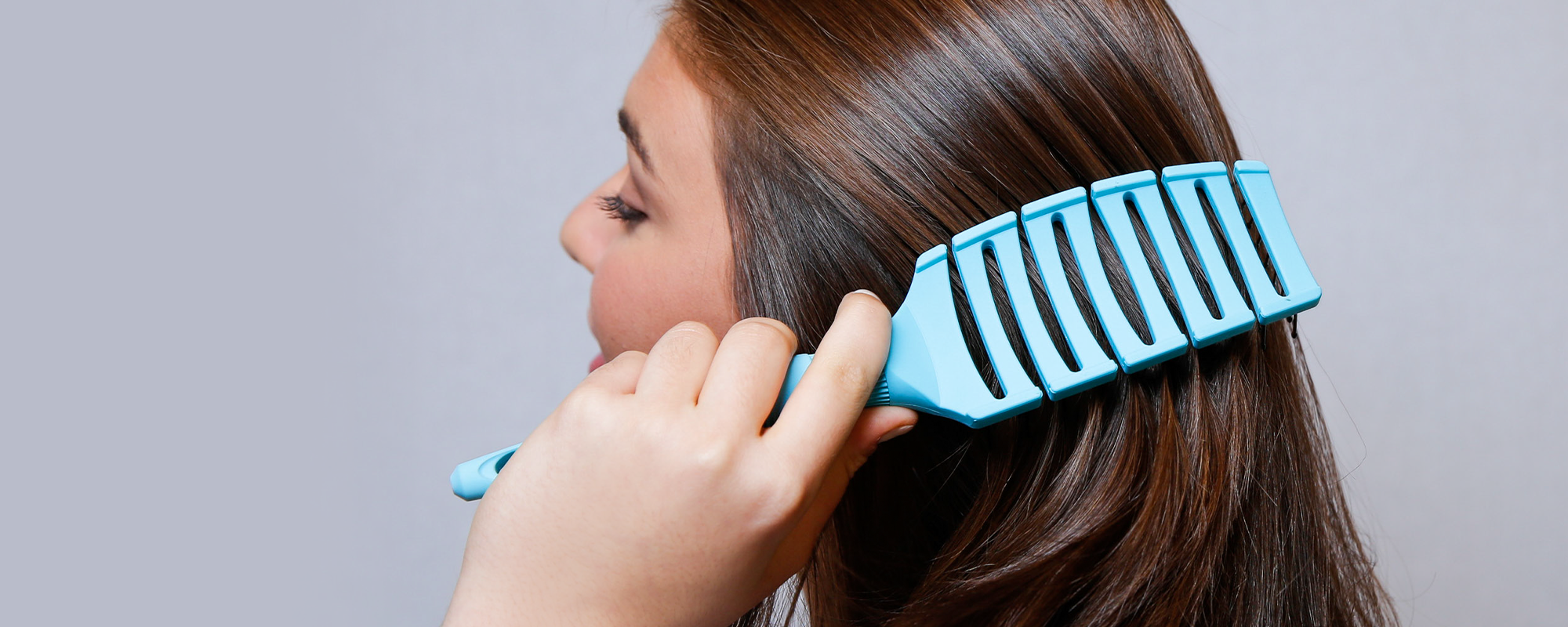 Person using a blue Flex Brush on their hair against a gray background